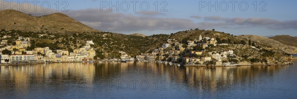 Panoramic view of a harbour town with reflecting buildings in the calm water. Mediterranean scenery with hills, Symi town, Symi, Dodecanese, Greek Islands, Greece, Europe