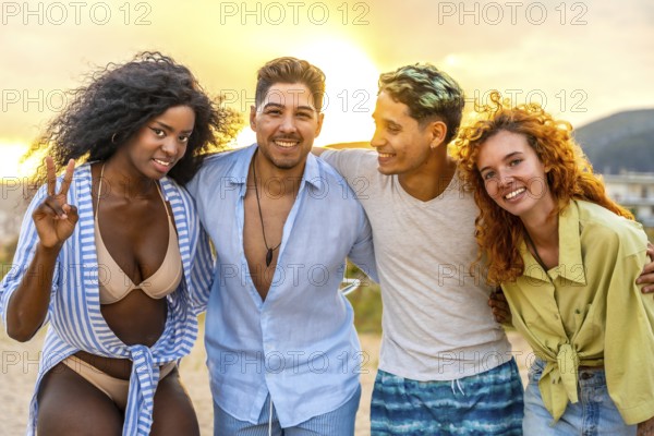 Four multi ethnic friends hug each other, enjoying a summer sunset at the beach, with one of them showing a peace sign