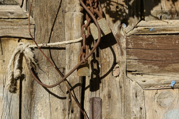 Old wooden door with rusty chains and locks, weathered in the sunlight, Symi Town, Symi, Dodecanese, Greek Islands, Greece, Europe