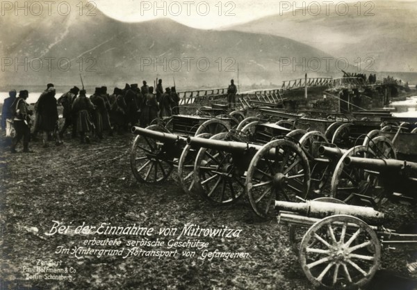 Serbian guns captured during the capture of Mitrovitsa. In the background, transport of prisoners, 1914 - 1918, World War I, reproduction of a war postcard