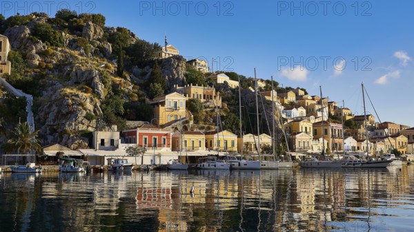 Picturesque building backdrop with boats in the water. Hilly landscape in the background, Mediterranean tranquillity, Symi town, Symi, Dodecanese, Greek Islands, Greece, Europe
