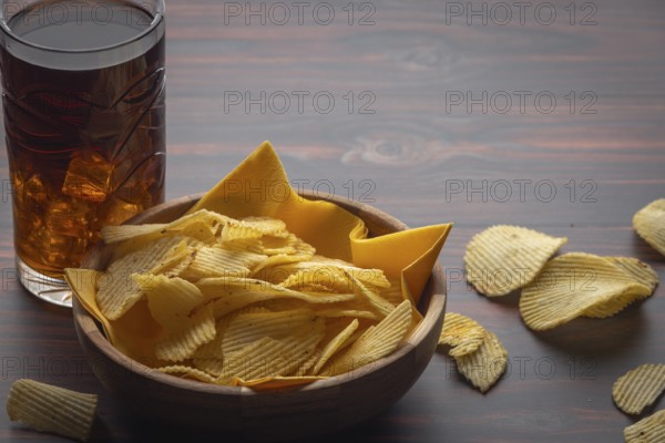 Wooden bowl with crisps and glass of cola on a table