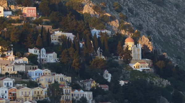 Beautiful mountain village with colourful houses and church surrounded by green vegetation in the sunlight, Symi Town, Symi, Dodecanese, Greek Islands, Greece, Europe