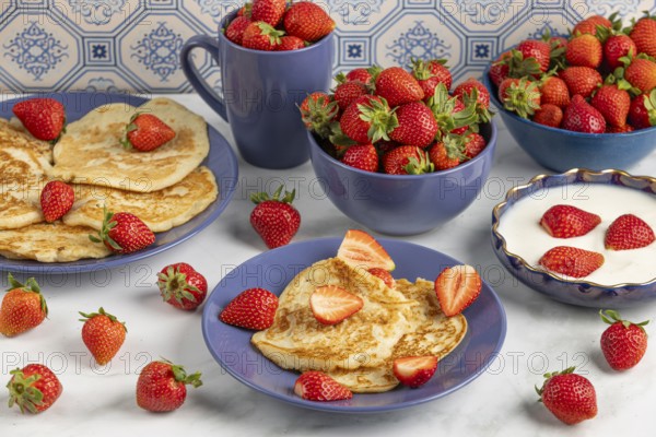 Pancakes and fresh strawberries on plates with yoghurt, blue crockery
