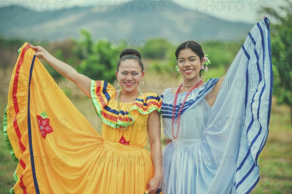 Portrait of two Hispanic women wearing cultural folkloric costume in a field. Two smiling Hispanic girls wearing cultural folkloric costumes outdoors