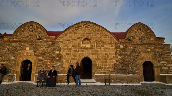 Old stone building in the evening light, people standing in front of the historic facade, Easter 2025, Church of the Dormition of the All-Holy God Bear, Kimisis tis Theotokou, Asklipio, Rhodes, Dodecanese, Greek Islands, Greece, Europe