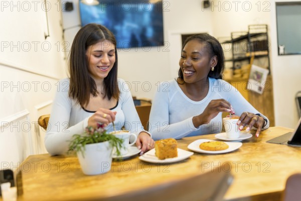 Two young women enjoying a coffee break, chatting and laughing together in a vibrant, modern cafe filled with natural light