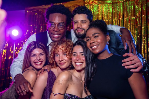 Group of cheerful elegant friends posing together for a photo at nightclub party with disco lights and gold tinsel curtain backdrop