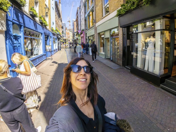 Happy tourist taking a selfie while walking in carnaby street, a popular shopping street in london's soho district, known for its fashion boutiques and trendy atmosphere