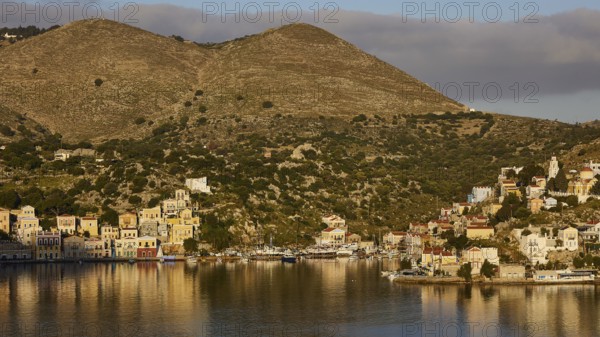 Houses on a green hill, illuminated by warm light, calm waters, Symi town, Symi, Dodecanese, Greek Islands, Greece, Europe