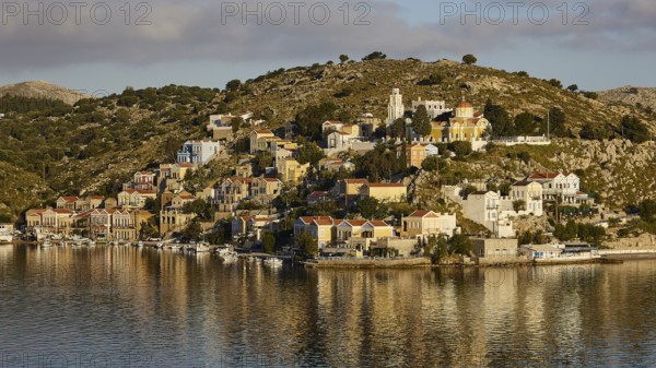 Pretty buildings on a hilltop island reflected in the water. Mediterranean atmosphere in the sunlight, Symi town, Symi, Dodecanese, Greek islands, Greece, Europe