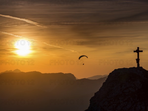 Paraglider flying next to the summit cross of the small Jenner at sunset, Reiteralpe in the background, Berchtesgaden National Park, Schönau am Königssee, Upper Bavaria, Bavaria, Germany, Europe