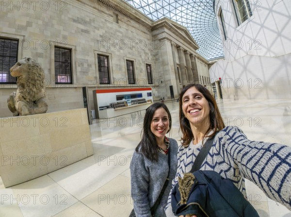 Two happy female tourists are taking a selfie with a fisheye lens at the british museum's great court in london, uk