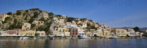 Colourful coastal houses reflect in the calm sea under a clear blue sky and create a picturesque atmosphere, Symi Town, Symi, Dodecanese, Greek Islands, Greece, Europe
