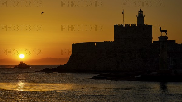 A boat glides in front of the silhouette of a fortress in the warm sunrise, dawn, Fort of Saint Nikolaos, Mandraki harbour, Rhodes town, Rhodes, Dodecanese, Greek Islands, Greece, Europe