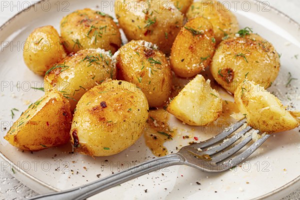 Half-eaten fried new potatoes, with butter and dill, on a white plate, with a fork, at home, no people