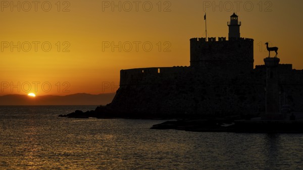 Majestic silhouette of a fortress against a glowing sunrise, dawn, Fort of Saint Nikolaos, Mandraki harbour, Rhodes town, Rhodes, Dodecanese, Greek Islands, Greece, Europe