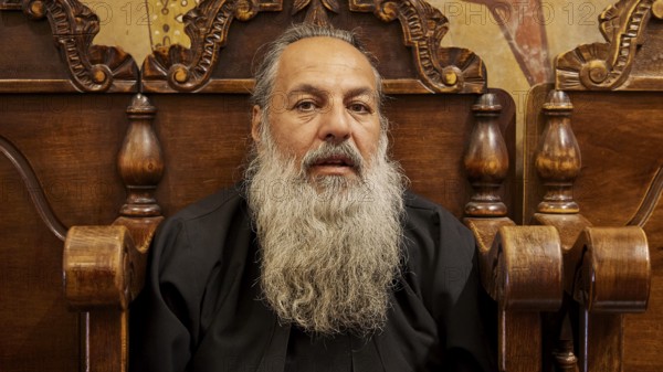 Portrait of a bearded man in black clothes, sitting on a wooden chair, Papas Nektarios, Monastery Thari, Moni Thari, near Gadouras Reservoir, lonely mountain region, Rhodes, Dodecanese, Greek Islands, Greece, Europe