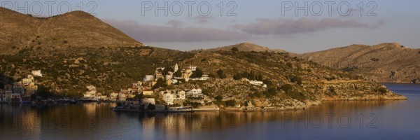 Island in a quiet bay, framed by mountains and bright sky in the morning light, Symi Town, Symi, Dodecanese, Greek Islands, Greece, Europe