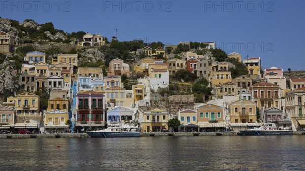 Row of colourful houses along the harbour with boats in the calm water, Symi Town, Symi, Dodecanese, Greek Islands, Greece, Europe