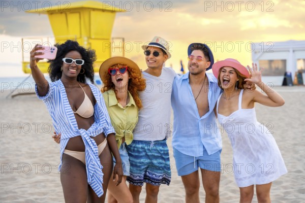 Group of multi ethnic friends taking a selfie on the beach in miami, florida, with lifeguard tower and sunset in background