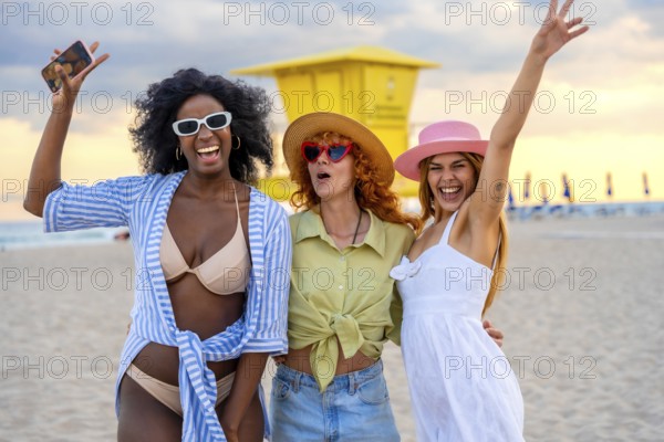 Three cheerful female friends taking a selfie on a beautiful beach at sunset, enjoying their summer vacation together