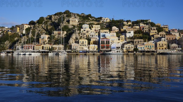 Colourful house front on the coastline with harbour and boat reflections in the water, Symi Town, Symi, Dodecanese, Greek Islands, Greece, Europe