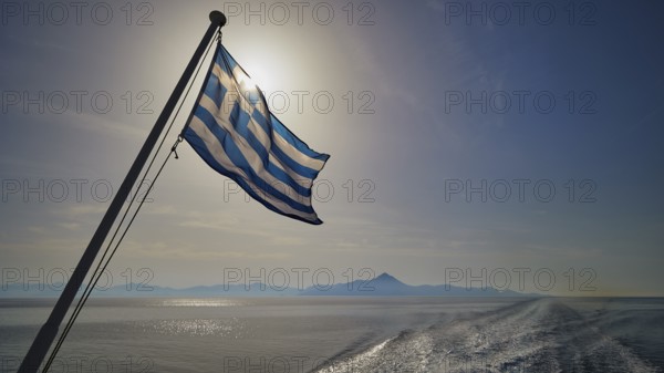 Greek flag in the foreground, over a widening sea under a blue sky, crossing Rhodes to Symi, ferry, Symi, Dodecanese, Greek Islands, Greece, Europe