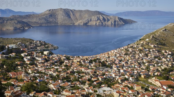 Sweeping views over a town nestled between mountains and calm sea, Symi Town, Symi, Dodecanese, Greek Islands, Greece, Europe