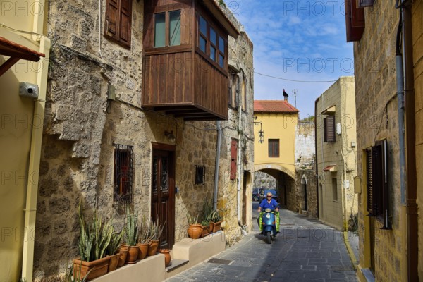 Narrow historic alley with a scooter driver and flower pots on a stone building, Rhodes Old Town, Rhodes, Dodecanese, Greek Islands, Greece, Europe