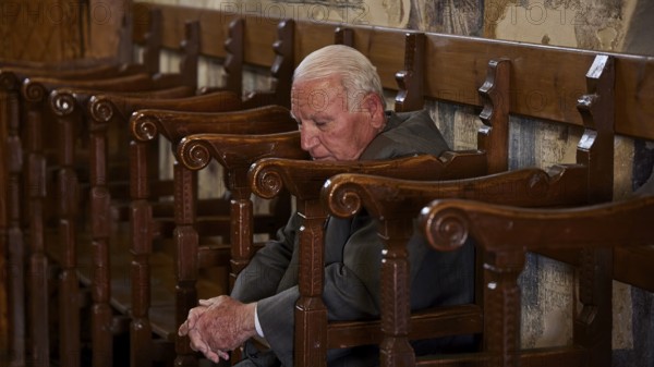 An elderly man leans back in a chair, his eyes closed as if he is sleeping, Easter 2025, Church of the Dormition of the All-Holy God Bear, Kimisis tis Theotokou, Asklipio, Rhodes, Dodecanese, Greek Islands, Greece, Europe