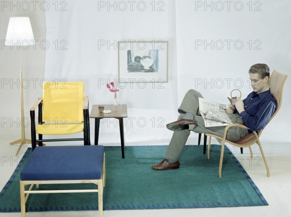 In the 1950s 1960s. A man is sitting comfortably in an armchair reading the newspaper and having a cup of tea and a cigarette. The furniture are made of wood and typical of the late 1950s early 1960s style. Sweden 1958 Conard ref BV109-6
