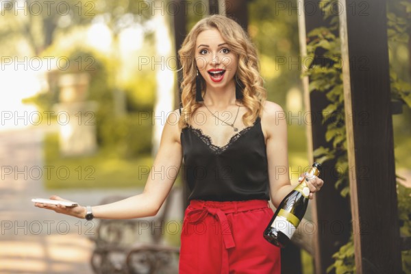 Happy young attractive white woman laughing joyfully, talking on the phone, holding a bottle of champagne and calling for a party. emotions lifestyle leisure relaxation positive communication