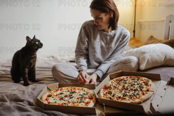 Woman in cozy setting with a cat and pizzas, appearing relaxed and comfortable indoors