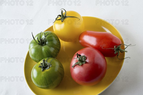 Different types of tomatoes on a yellow plate, green zebra tomatoes and raspberry tomatoes