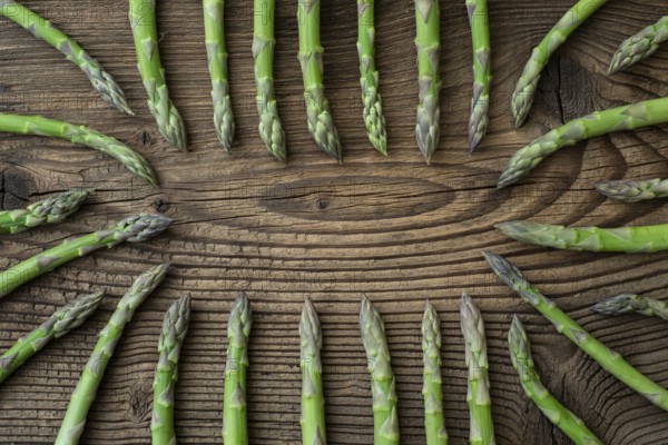 Raw garden asparagus stems. Fresh green spring vegetables on wooden background. (Asparagus officinalis)