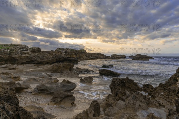 A rocky cove and sandy beach under an expressive sunset sky on the rugged west coast of Sardinia