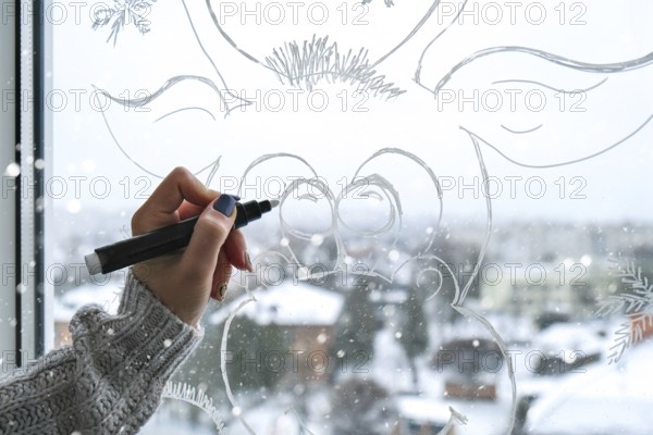 Female hand painting Christmas deer painted on window glass. Christmas winter decor on the window glass. White pattern of deer. Snow art tracery window on holiday season. Diy. Hygge home