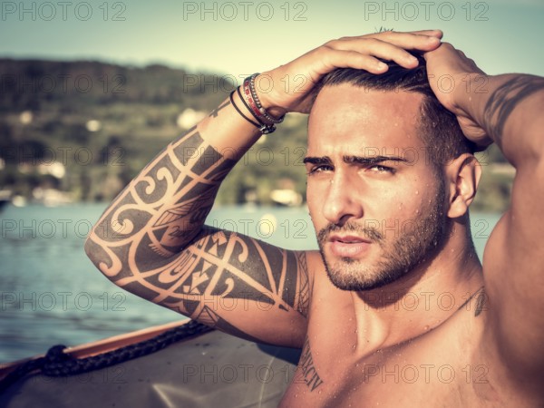 Portrait of young bearded handsome man with tattooed body looking sexually at camera sailing in boat