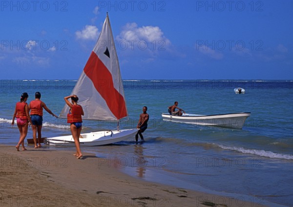 Beach, helper pulls sailboat into the water for 3 tourists, Playa Dorada, Dominican Republic, Central America