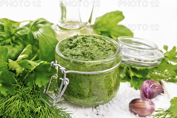Sauce of dill, parsley, basil, cilantro, other spicy herbs, garlic and vegetable oil in a glass jar, coarse salt on wooden board background
