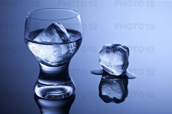 An elegant shot glass with vodka and ice and a melting ice cube on a reflective surface