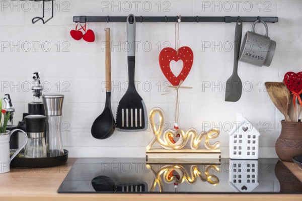 The interior of the kitchen in the house is decorated with red hearts for Valentine's Day. Decor on the table, stove, utensils, festive mood in a family nest