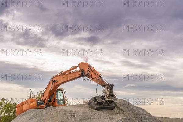 Heavy orange excavator with big bucket working on top of a ballast pile