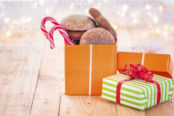 Ton of colorful gifts, one opened full with gingerbread and Xmas candies, laid on a wooden background, surrounded by blurred Christmas lights