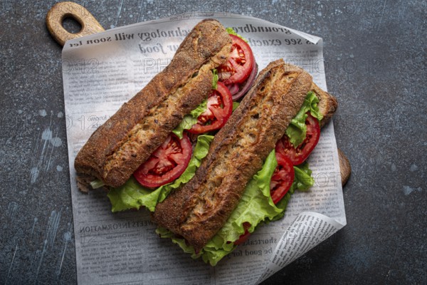 Two dark ciabatta sandwiches with green salad, ripe red tomatoes, onion and tuna on rustic concrete stone background top view. Vegetable vegetarian sandwiches, healthy snack or lunch, food photography, food photography