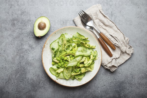 Healthy vegan green avocado salad bowl with sliced cucumbers, edamame beans, olive oil and herbs on ceramic plate top view on grey stone rustic table background, food photography, food photography
