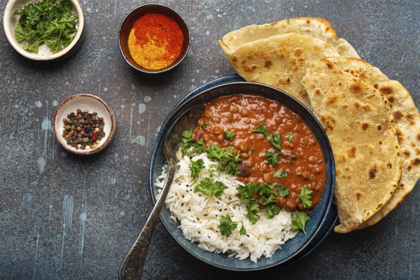 Traditional Indian Punjabi dish Dal makhani with lentils and beans in black bowl served with basmati rice, naan flat bread, fresh cilantro and spoon on blue concrete rustic table top view, food photography, food photography