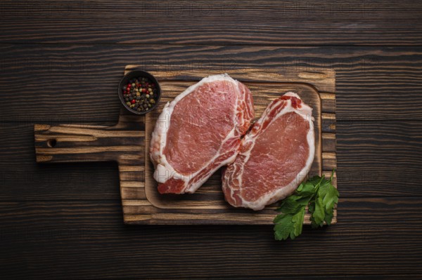 Cut raw meat pork steaks with seasonings on kitchen cutting board, rustic wooden background top view, ready for BBQ. Pork loin chops, food photography, food photography