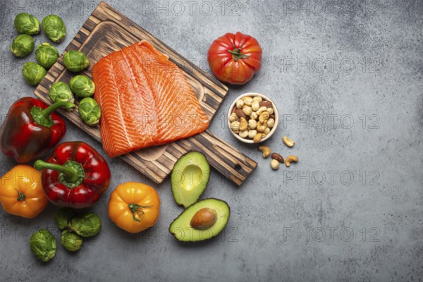 Fresh raw salmon fillet on wooden cutting board, organic bio vegetables and nuts on rustic stone grey background top view. Ingredients full of vitamins for healthy diet and nutrition, space for text, food photography, food photography